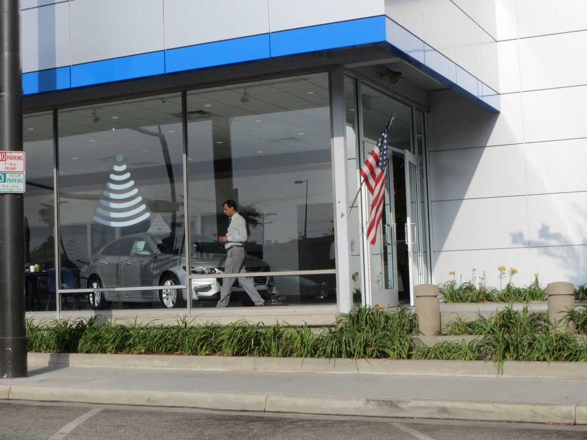 Person walking inside of a car dealership taken through the front window